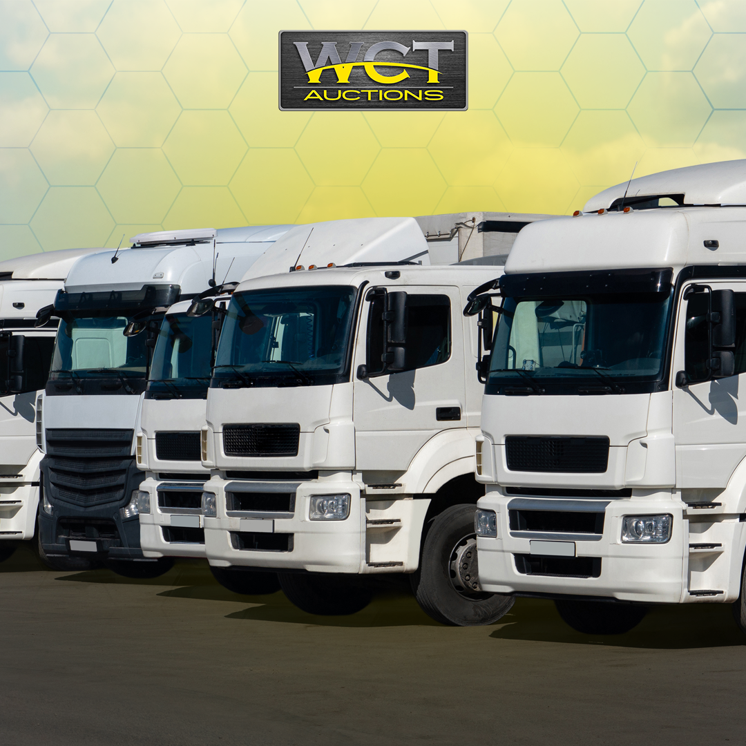 Row of white commercial trucks with WCT Auctions logo banner